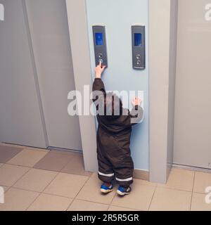 A small child presses the elevator call button. Baby reaches for the elevator button in a residential building. Kid aged about two years (one year ten Stock Photo