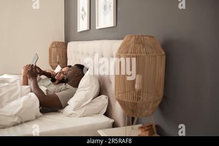 Smiling multiracial couple using a digital tablet in bed Stock Photo
