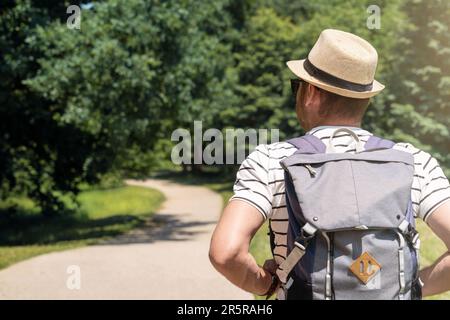 Rear view man with backpack and hat walking outdoors in the park in summer. Stock Photo