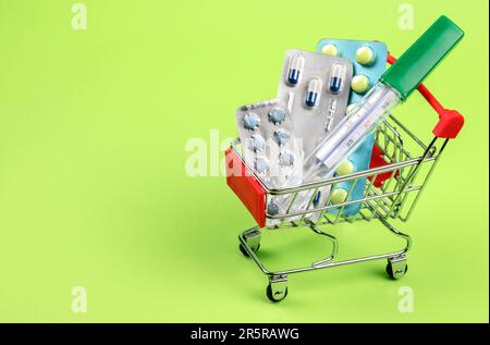 Thermometer, pills, tablets and vitamins in a shopping cart on green background. Concept: shopping and delivery of medicines Stock Photo