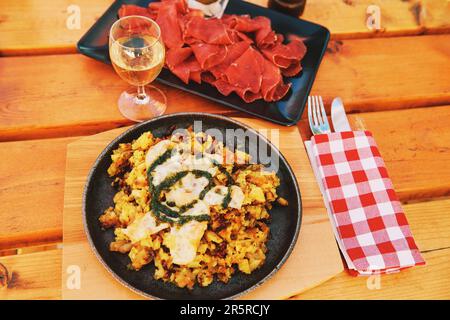 Traditional swiss plate rosti with melted cheese and green sauce pesto, served with white vine and famouse valais cold meet plate Stock Photo