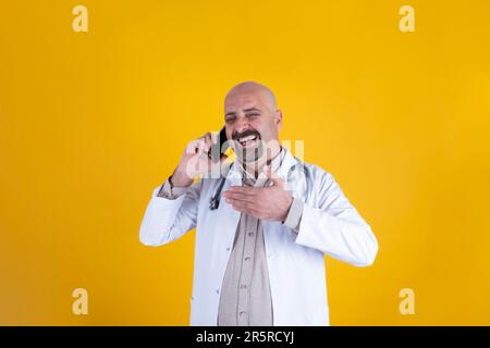 Bald caucasian male doctor talking on the phone. Happy physician wearing hospital uniform, stethoscope. Lol. Speaking with friend, cheerful face. Stock Photo