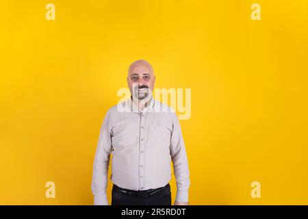 Caucasian middle aged portrait of smiling man. Front shot of father figure male standing over isolated yellow background, copy space. Bald bearded guy Stock Photo