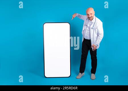 Full size doctor standing near big smartphone with empty screen. Hospital web page, medical app, tele medicine concept idea. Advertising template. Stock Photo