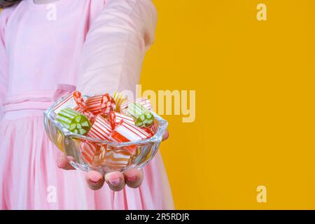 Little girl holding bowl of hard candies. Yellow studio background copy space. Traditional Ramadan or Ramazan feast greeting concept. Stock Photo