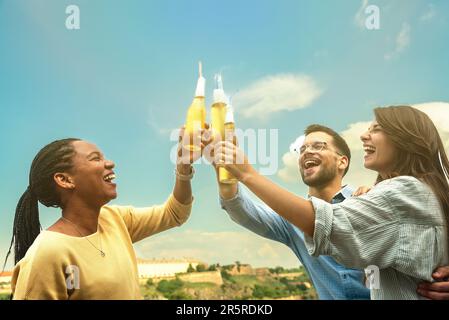 Group of happy young multiracial friends colleagues freelancers in casual clothes drinking cold beer and dancing together while having party on buildi Stock Photo