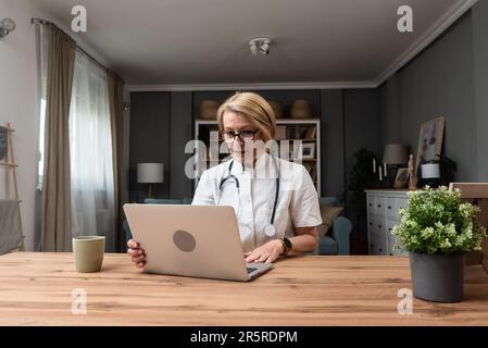 Mature woman doctor explaining about medicine through video call on laptop. Female health care worker talking with patient on web cam on computer from Stock Photo