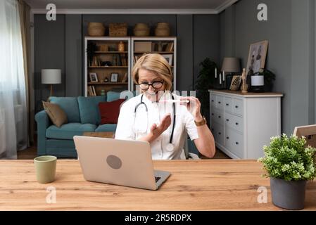 Mature woman doctor explaining about medicine through video call on laptop. Female health care worker talking with patient on web cam on computer from Stock Photo