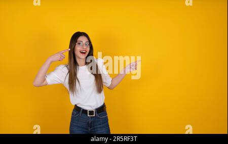 Portrait of excited happy woman pointing fingers aside copy space. Recommend, offer advertising concept idea image. Isolated yellow background. Stock Photo