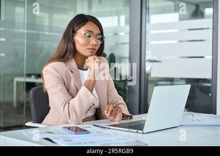 Serious busy young business woman looking at laptop thinking of market risks. Stock Photo