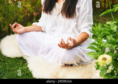 Middle age woman meditating in green garden, sitting on sheep skin Stock Photo