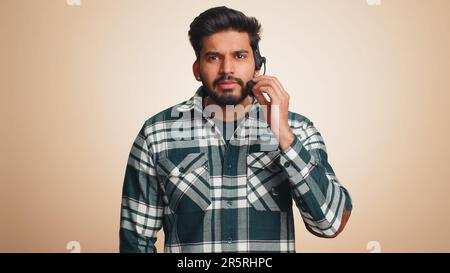 Smiling indian man wearing headset, freelance worker, call center or support service operator helpline, having talk with client or colleague, communication support. Handsome guy on beige background Stock Photo