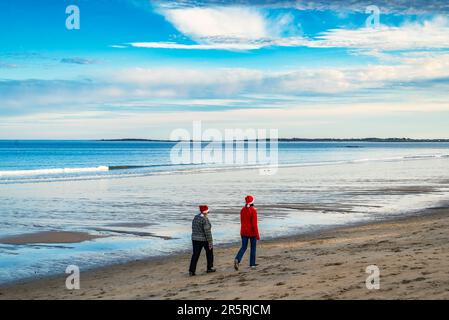 Rear view of a couple of women, with Santa Claus hat, walking along the ocean shore Stock Photo