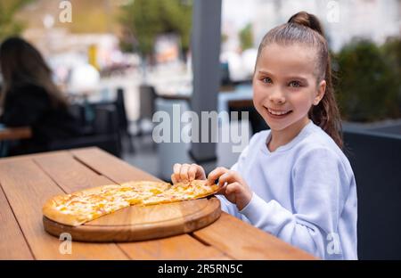 child girl eat pizza in cafe, looking at camera and smiling in terrace pizza restaurant Stock Photo