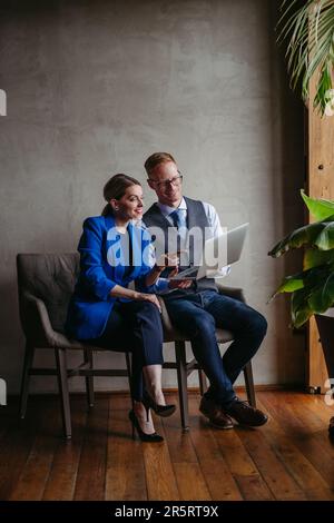 Two colleagues sitting near window and working on notebook in modern office full of plants. Stock Photo