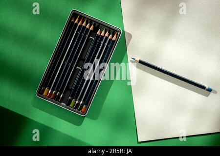 Still life with a box of pencils, a sheet of paper and a pencil on a green background Stock Photo