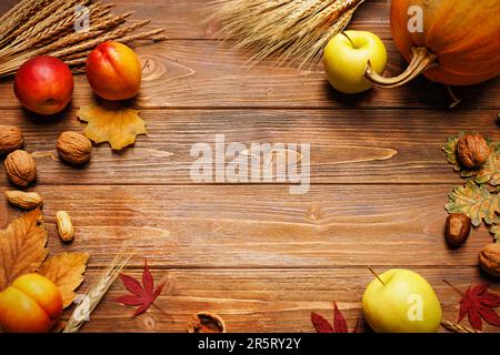 Autumn still life with pumpkin, apple, peach, wheat and barley ears, maple and oak leaves, walnuts and peanuts on a wooden background Stock Photo