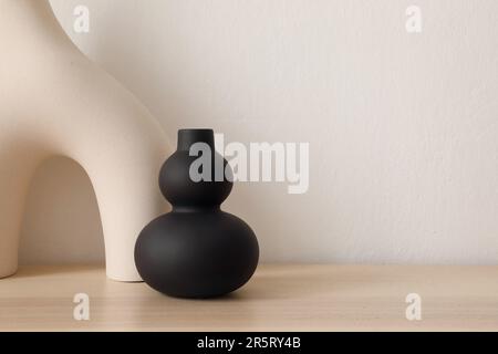 Set of modern ceramic vases of geometric organic shape on wooden table. Modern black sculpture. Beige wall. Abstract trendy artistic background, web Stock Photo