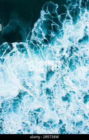 A powerful wave of clear blue water crashing against the surface of the ocean, creating a white foam-filled crest of spray Stock Photo