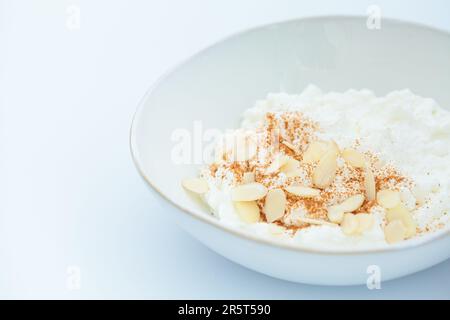 Cottage cheese with cinnamon and almonds in a white bowl, white background. Healthy protein breakfast concept. Stock Photo