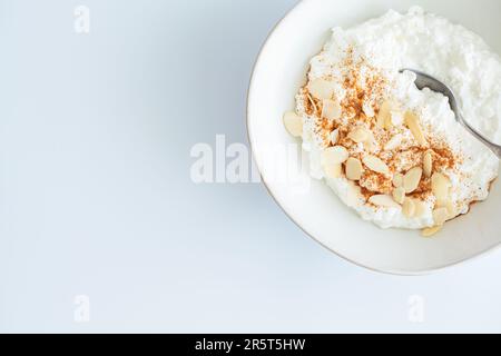 Cottage cheese with cinnamon and almonds in a white bowl, white background, top view. Healthy protein breakfast concept. Stock Photo