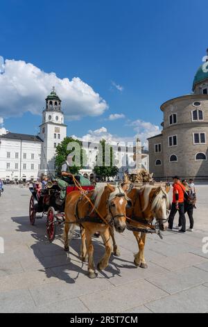 Salzburg, Austria - 06.01.2023: traditional sightseeing horse driven carriage with tourists ion the Residenzplatz of Salzburg . Stock Photo