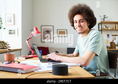 Young man talking to artificial intelligence while working online on laptop sitting at table in the room Stock Photo