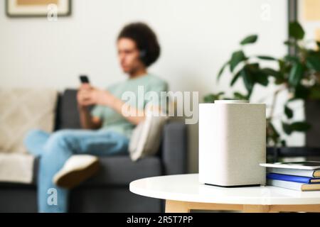 Close-up of smart speaker standing on coffee table in the room with man using smartphone in background Stock Photo