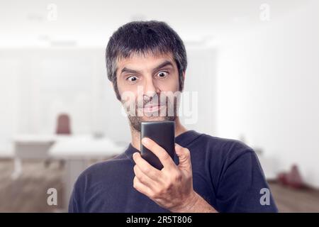 Mature man with dark hair wearing a surprised expression while looking at his mobile phone in an office environment. Stock Photo
