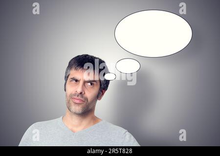 Thoughtful-looking man in the foreground, with a gray background adorned with white bubbles representing thoughts and creativity. Stock Photo