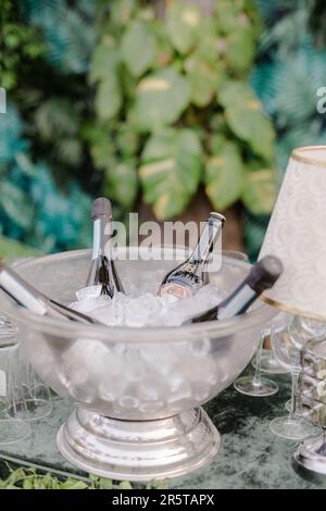 Two full bottles of red wine in a wooden bowl on a white linen-covered table, positioned outdoors in natural light Stock Photo