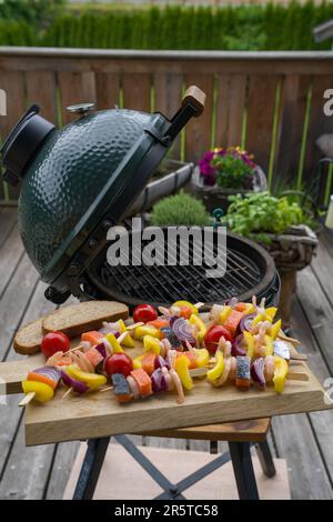 raw grilling shrimps skewers with salmon and vegetables on a wood board for grilling on a charcoal grill on the balcony at a summer day Stock Photo