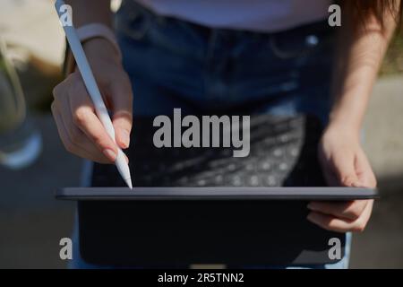 Creative young girl drawing an illustration with a stylus pen on a tablet computer. Freelance graphic designer female making a sketch outdoor Stock Photo