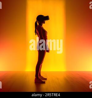 A young female standing alone in a dark room wearing a virtual reality headset Stock Photo