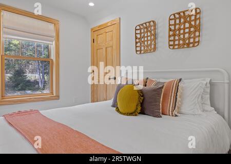 A made bed in a cozy bedroom featuring a set of decorative pillows on top Stock Photo
