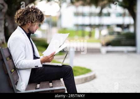 African american middle aged entrepreneur working on laptop and reading documents outdoors, side view Stock Photo