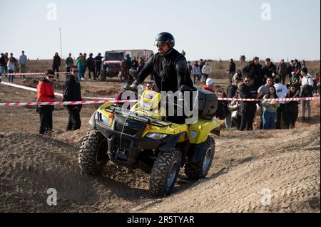 A fat man dressed in black riding a yellow Suzuki Kingquad quad bike through the off-road area Stock Photo