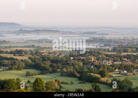 Dawn light falls on the misty landscape of the Vale of Evesham as seen from Broadway Hill on the Cotswold Edge in Worcestershire. Stock Photo