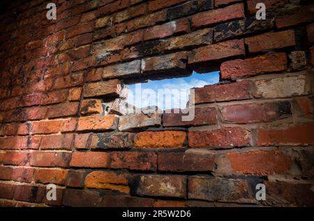 A hole in an old brick wall revealing a blue sky. Stock Photo
