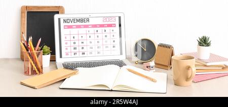 Calendar for November 2023 on screen of laptop, notebook, alarm clock and office supplies at workplace Stock Photo