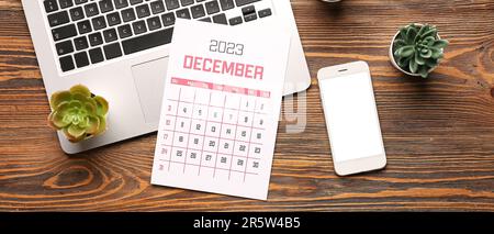 Calendar for December 2023, modern laptop and mobile phone on wooden background Stock Photo