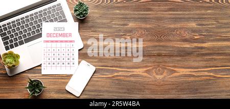 Calendar for December 2023, modern laptop and mobile phone on wooden background with space for text Stock Photo