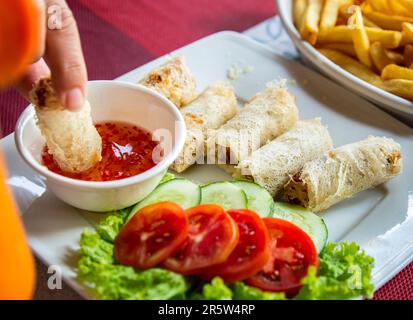 Vietnamese vegetable spring rolls with tomato, cucumbers and red chilli sauce placed on restaurant dining table. Stock Photo