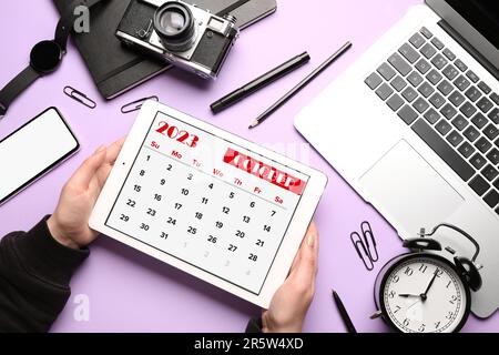 Woman holding tablet computer with calendar near different gadgets on lilac background Stock Photo
