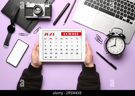 Woman holding tablet computer with calendar near different gadgets on lilac background Stock Photo