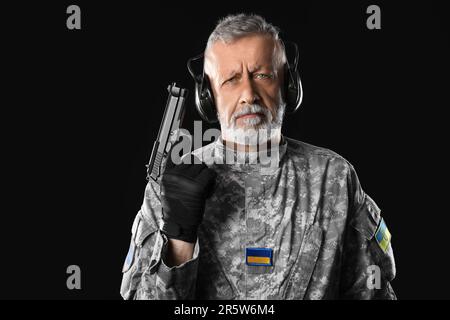 Ukrainian soldier in headphones with gun on dark background Stock Photo
