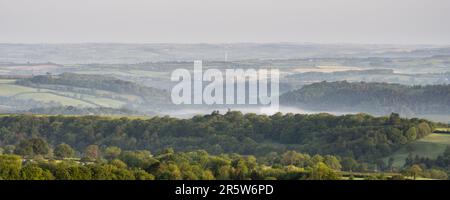 Morning mist rises from the woodland of the Lyd Valley in the rolling landscape of West Devon and Cornwall as viewed from Brent Tor hill on the edge o Stock Photo