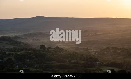Mist rises from the valleys around Lydford and North Brentor under the hills of Dartmoor at sunrise  in West Devon, as seen from Brent Tor. Stock Photo