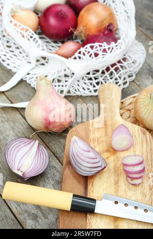 Wooden board and string bag with different kinds of onion on white tile ...