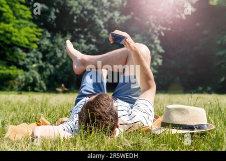 Man relaxing on green lawn in the city park and using his mobile phone. Stock Photo